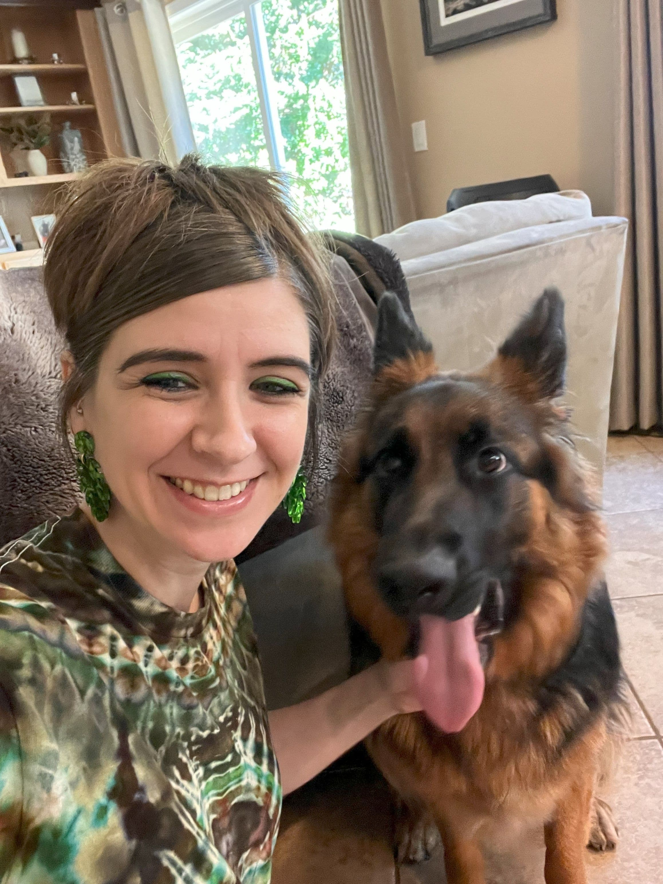 Woman with green earrings smiling with a German Shepherd dog indoors.